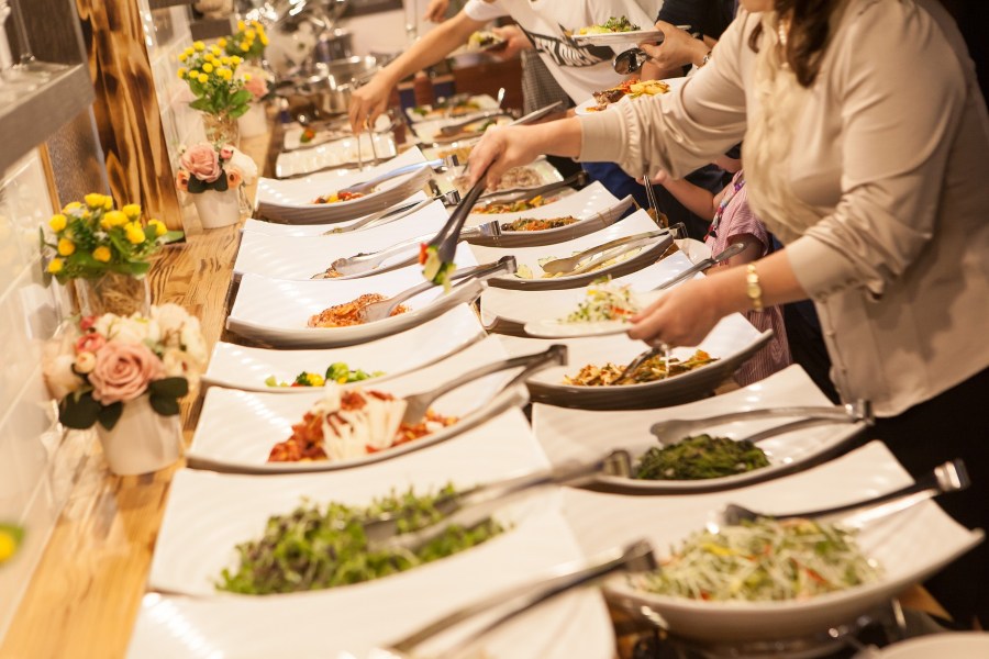 Woman in beige blouse taking food from buffet