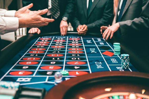 men sitting around a roulette table placing bets men sitting around a roulette table placing bets