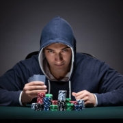 an ominous looking man wearing a hoody at a poker table
