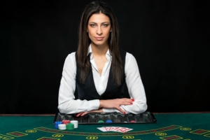 White female dealer sitting arms folded at blackjack table