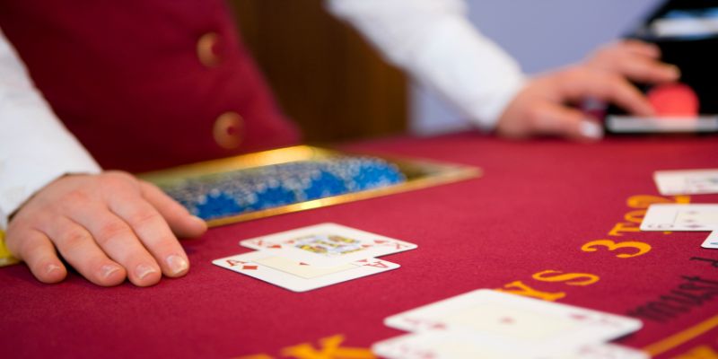Burgundy casino table with dealer standing palms down, with casino cards laid face up